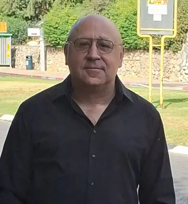 A man in a black shirt and glasses standing outdoors with one hand in his pocket.