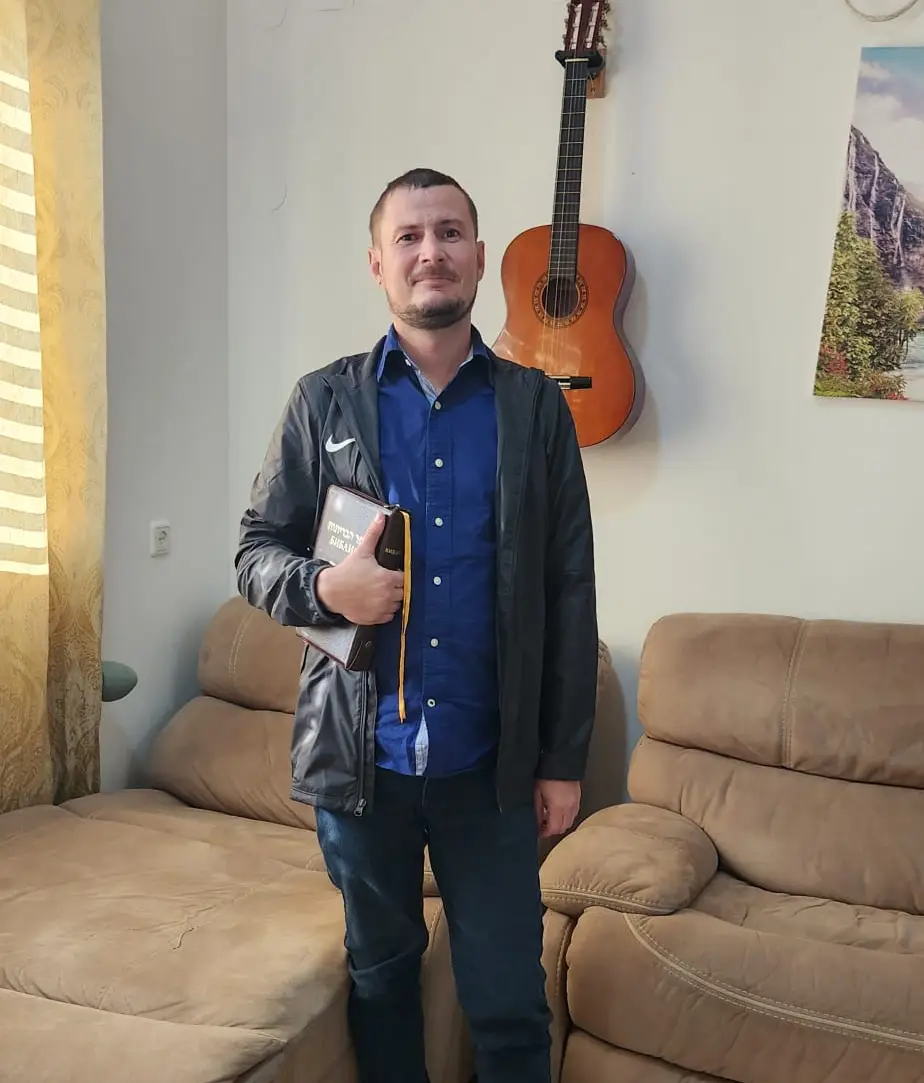 Nataniel standing with a book in his hands, with a guitar hanging on the wall in the background.