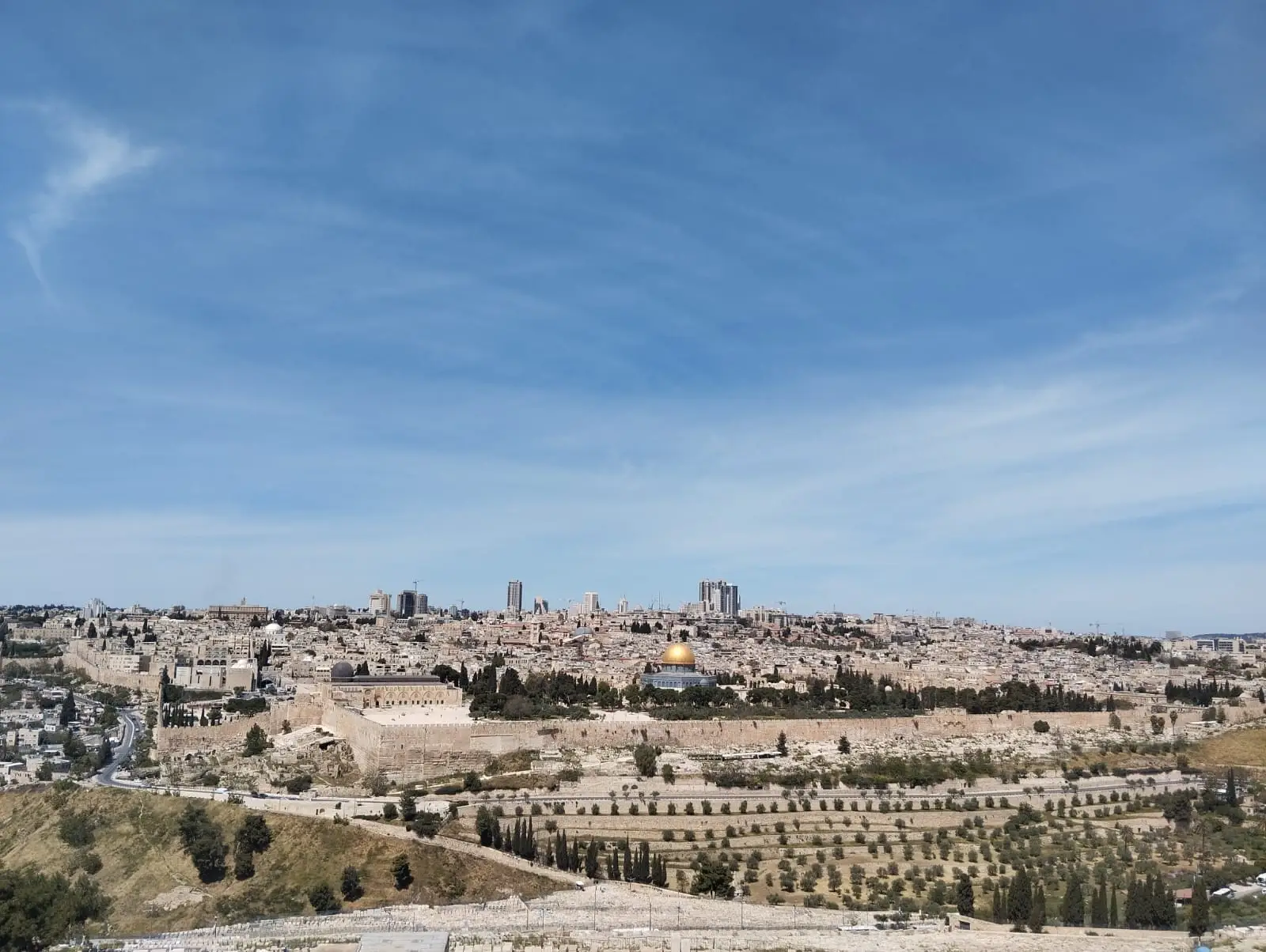 Panoramic view of Jerusalem Old City walls and the golden Dome of the Rock under a bright blue sky.
