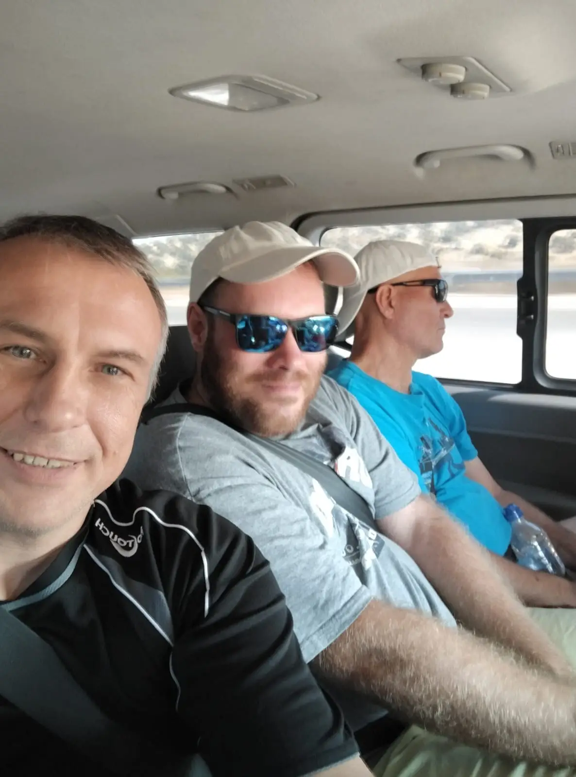 Three men wearing casual clothes and baseball caps sitting inside a van on our Lake Kinneret ministry trip.