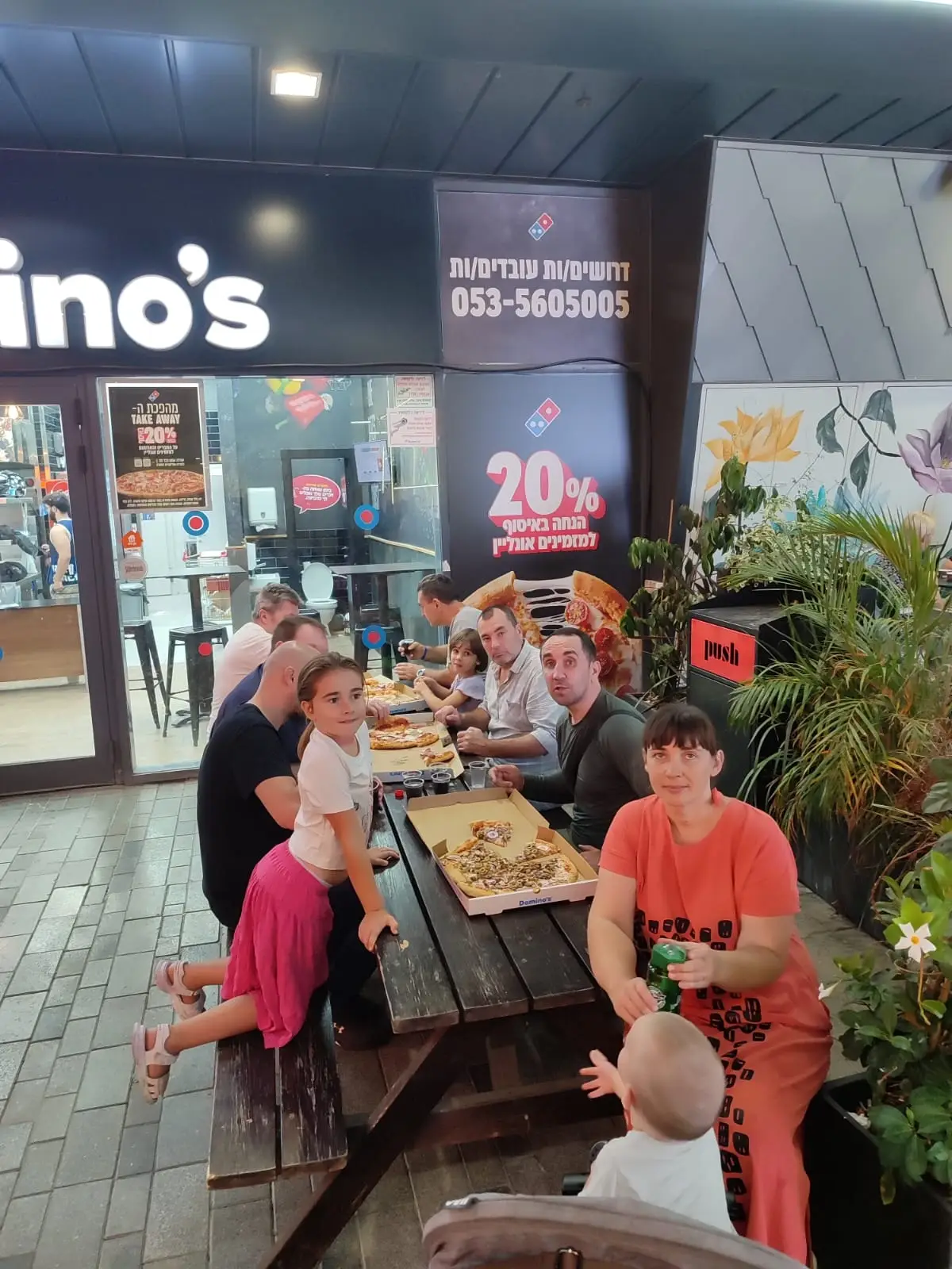 People sitting around outdoor wooden tables with pizza during a Church family birthday celebration.