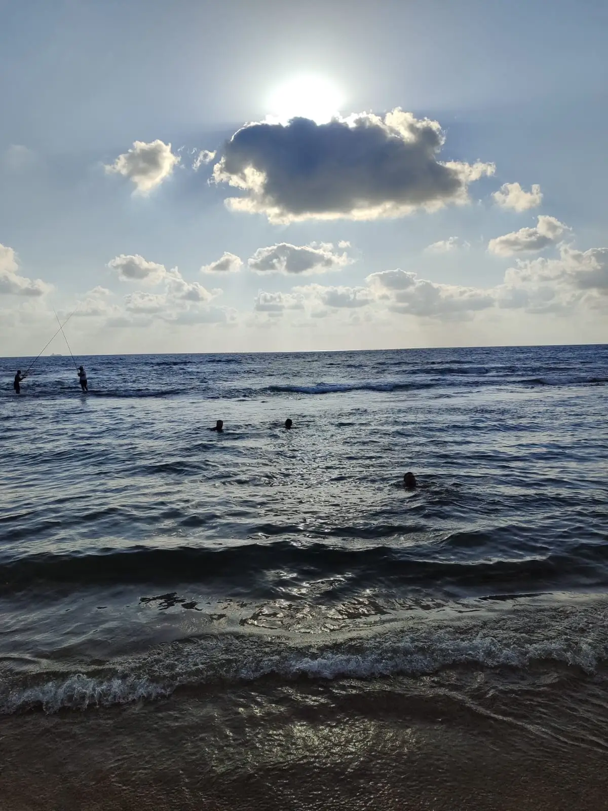 People swimming in sea waves under cloudy sky during an Akko beach church fellowship trip.